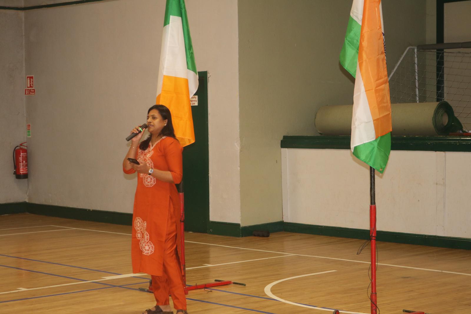 Host addressing the gathering beside the Indian and Irish flags